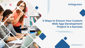 A group of three people are sitting at a table, looking at a laptop. The people are all wearing business attire and appear to be in their 30s or 40s. The laptop is open to a website with the title "5 Ways to Ensure Your Custom Web App Development Project is a Success."